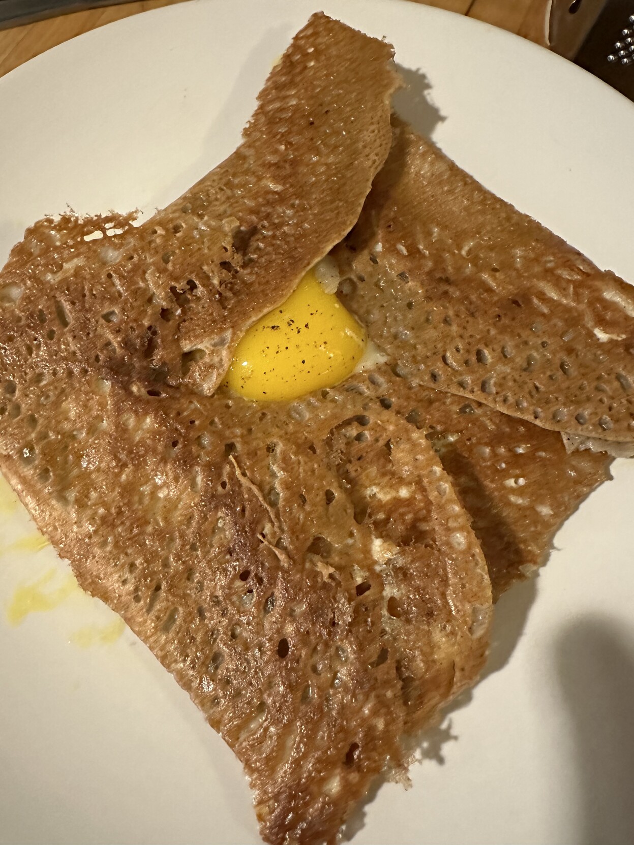 Picture of a Galette, it’s brown, thin and crispy with an egg yolk in its center.